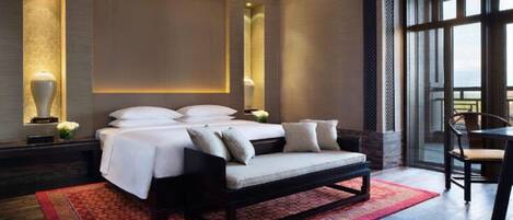 A modern hotel room with a large bed, a sofa, a dining table, and a view of the outdoors.