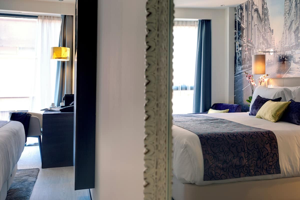 Ein Hotelzimmer mit einem großen Bett, einem Schreibtisch mit Computer und Blick auf eine belebte Straße.