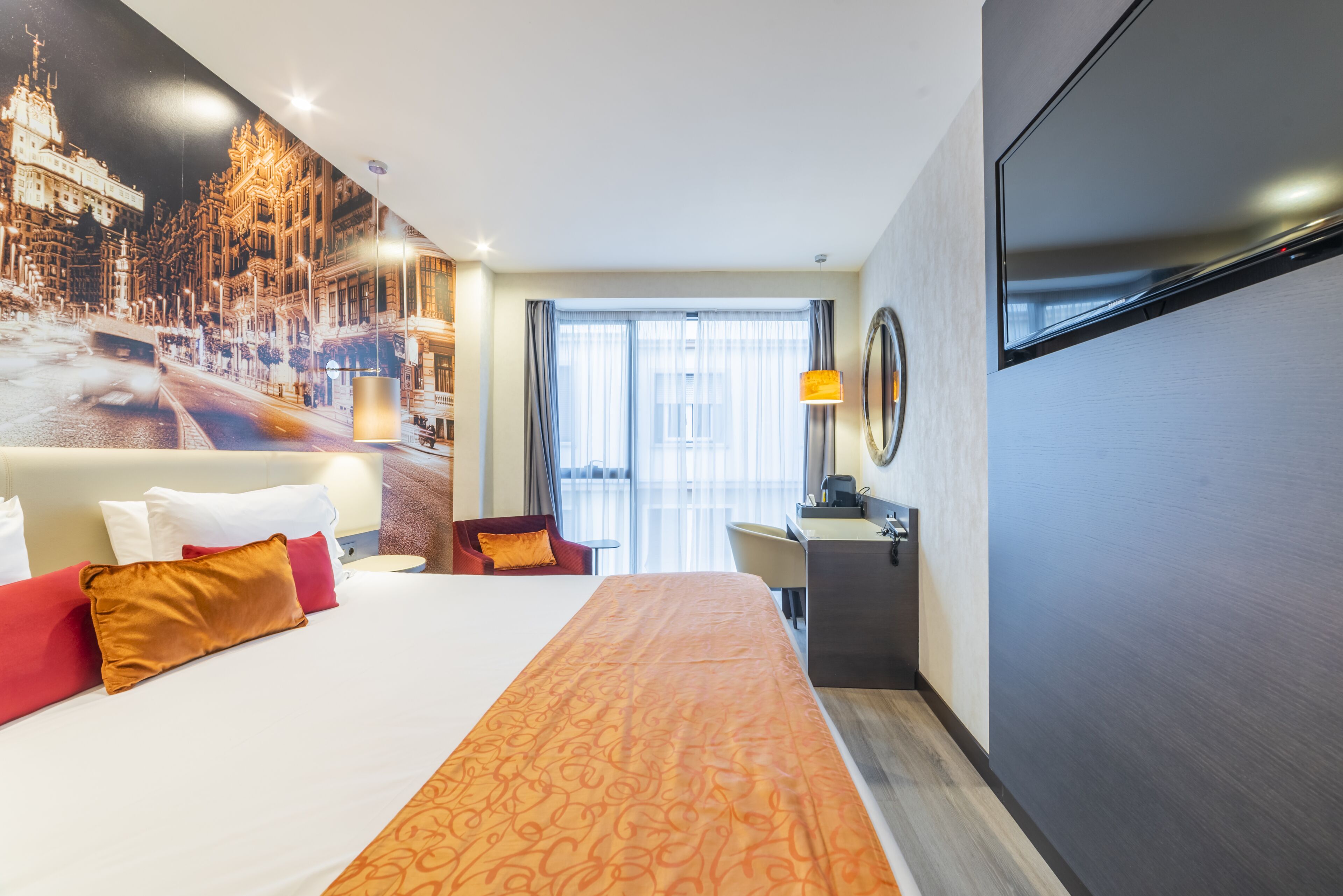 A hotel room with a large bed, a desk, a chair, and a TV.