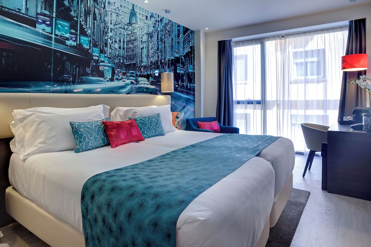 Ein modernes Hotelzimmer mit einem großen Bett, einem Schreibtisch und Blick auf die Stadt durch das Fenster.