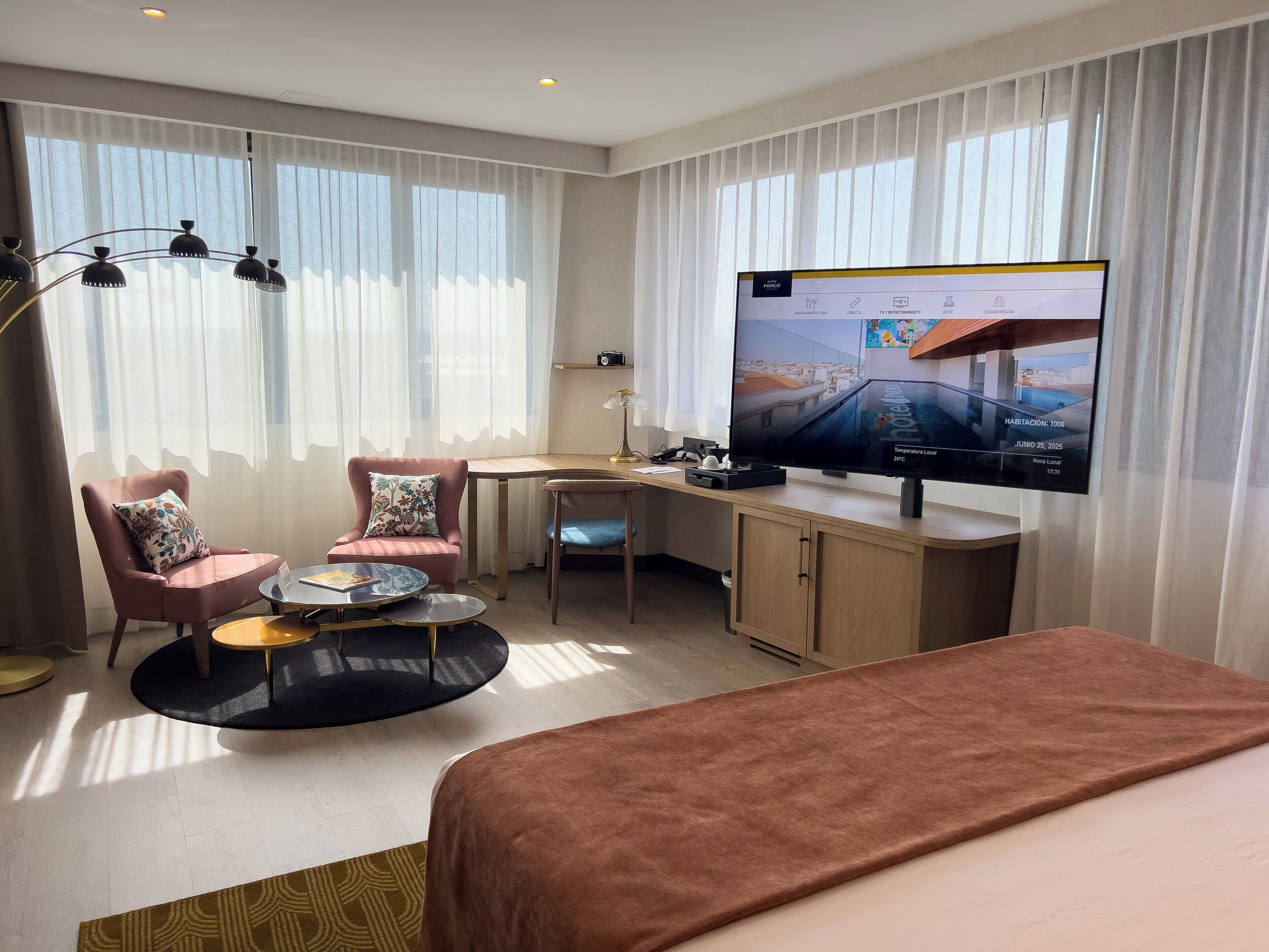 Une chambre d’hôtel équipée d’un lit, d’un bureau, d’une chaise, d’une télévision et d’une fenêtre avec des rideaux.