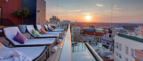 Una terraza en la azotea con sillones de descanso y vistas a la ciudad al atardecer.
