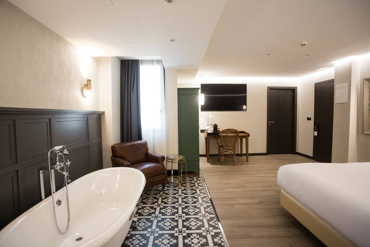 Ein modernes Hotelzimmer mit einer großen Badewanne, einem Bett, einem Schreibtisch und einem Fernseher.