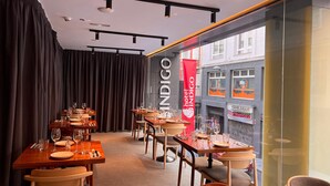 L’intérieur d’un restaurant, avec des tables dressées pour le service, une banderole rouge et une vue sur la rue.