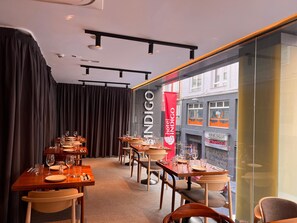 A restaurant interior with tables set for dining, a red banner, and a view of the street outside. - Hotel Indigo Madrid - Gran Via by IHG (Madrid)