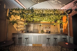 Zona de bar con mostrador, taburetes y plantas colgantes.