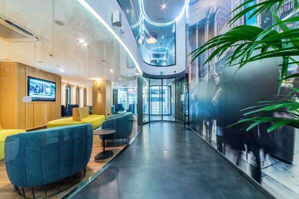 A modern lobby with a curved glass wall, seating areas, and a television screen.