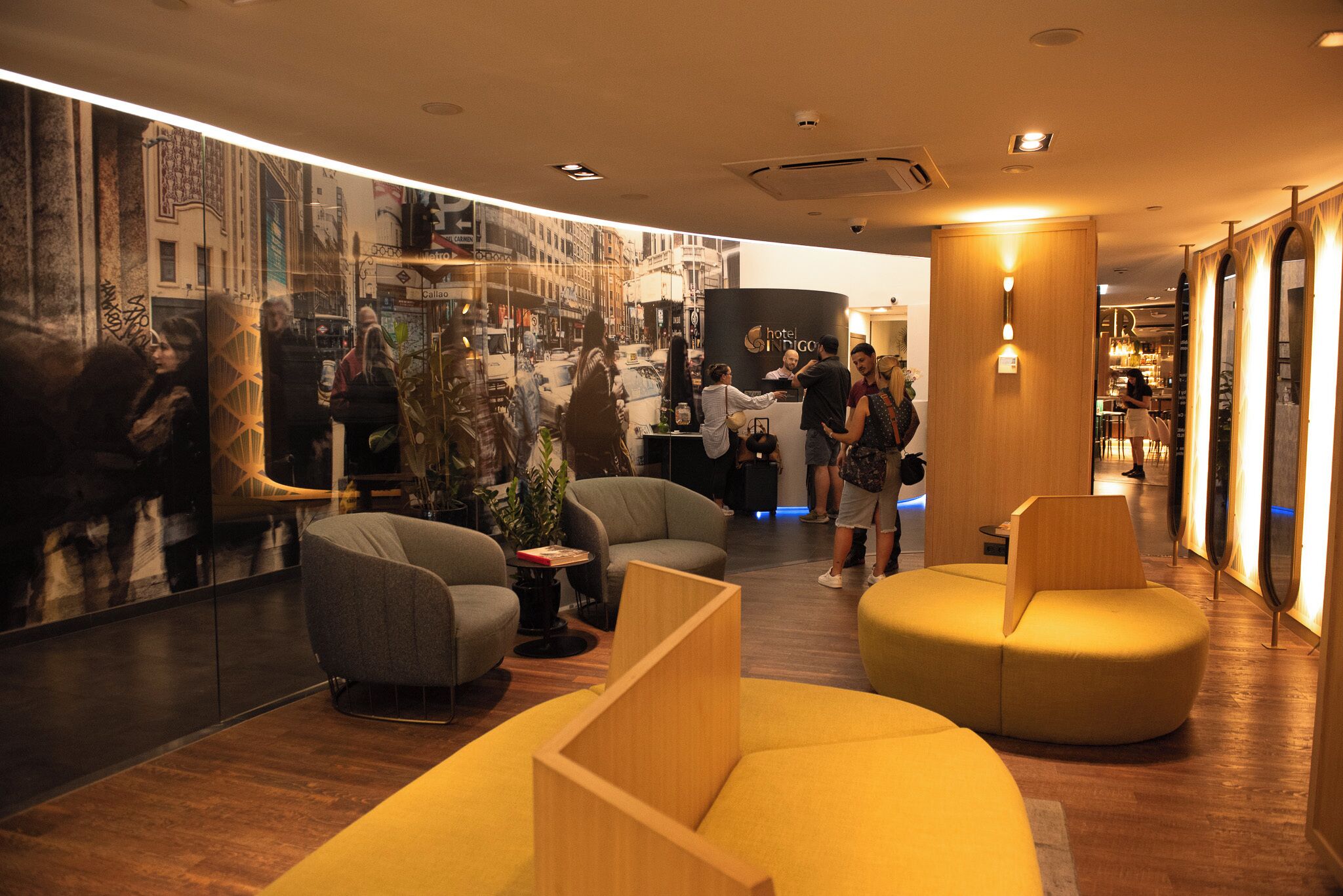 A hotel lobby with modern furniture, a reception desk, and a large cityscape mural on the wall.