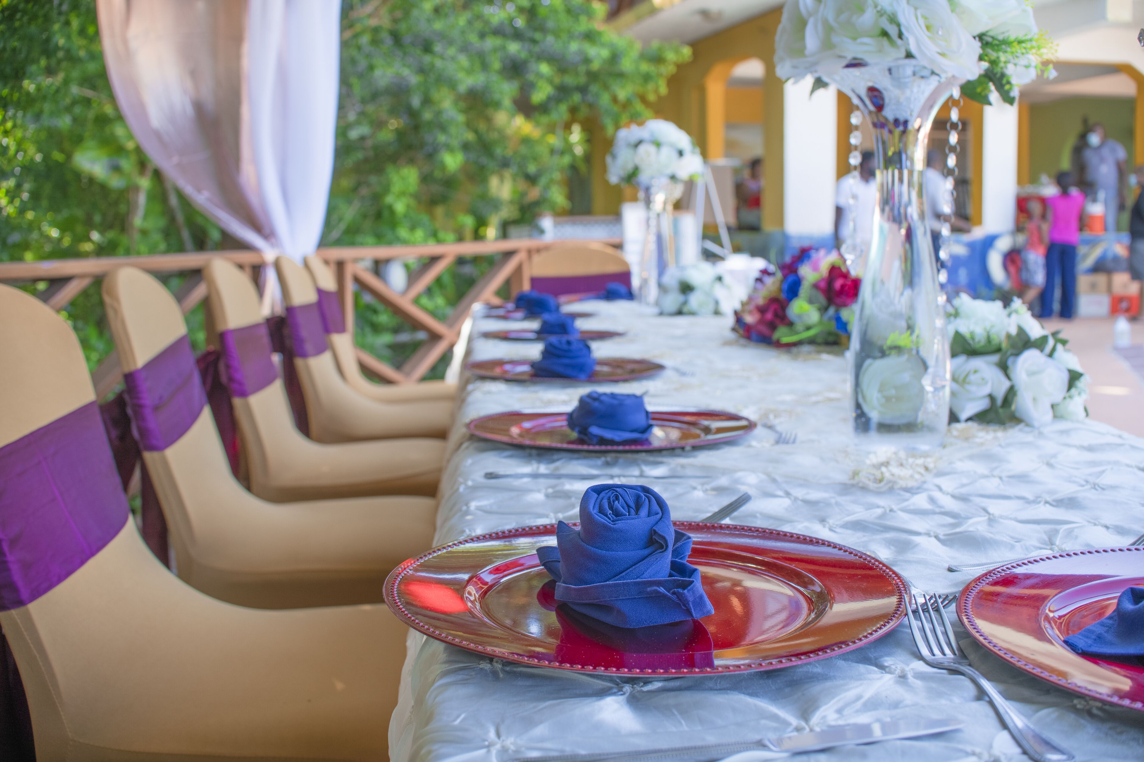 A table set with red and clear plates, blue napkins, and white flowers.