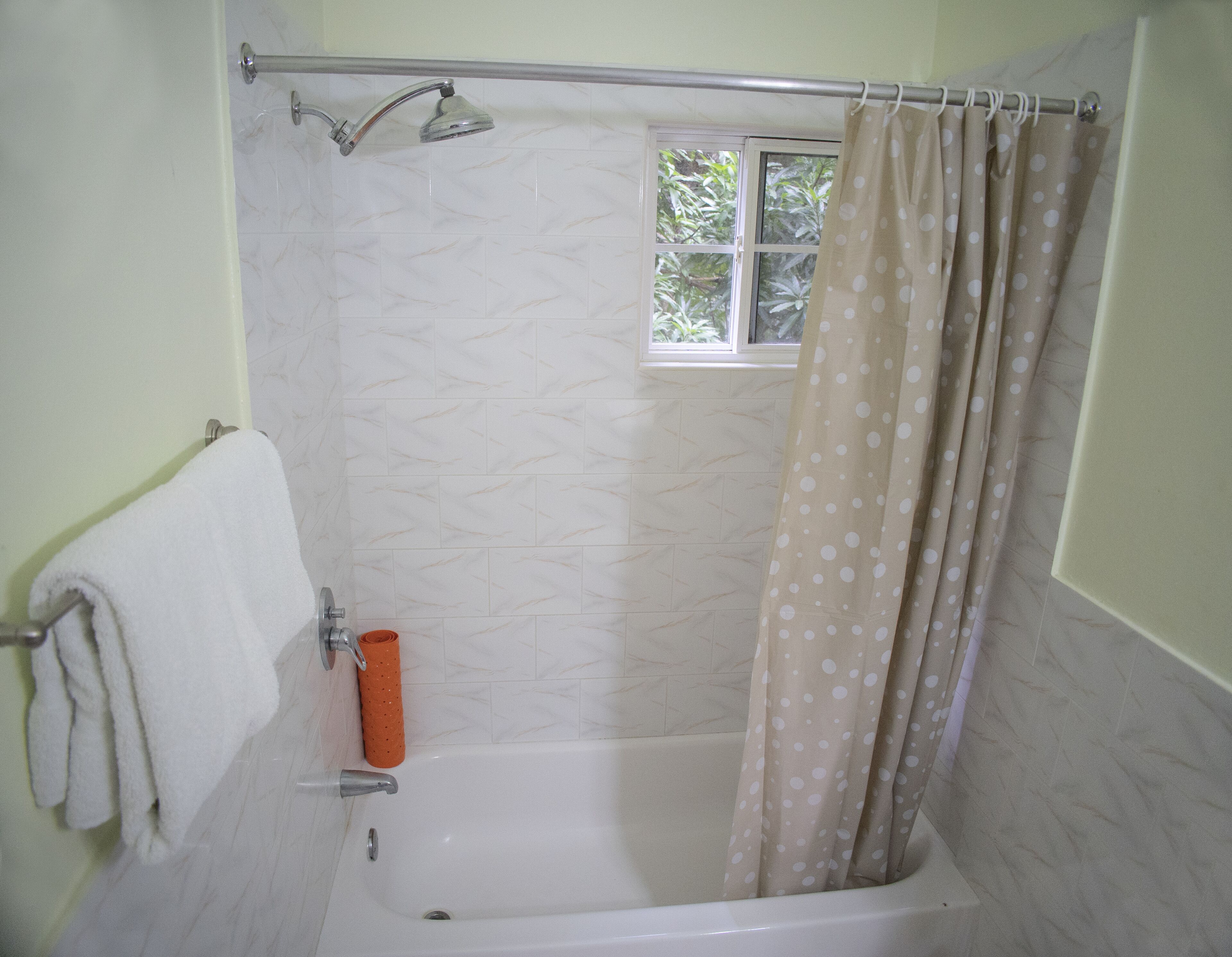 A bathroom with a bathtub, a shower curtain, and a window.
