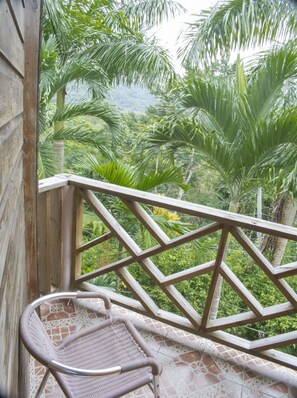 Un balcón de madera con una silla de mimbre, con vistas a un exuberante jardín con plantas tropicales.