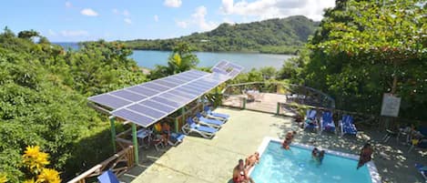 A swimming pool with solar panels, lounge chairs, and a view of a lake and hills.