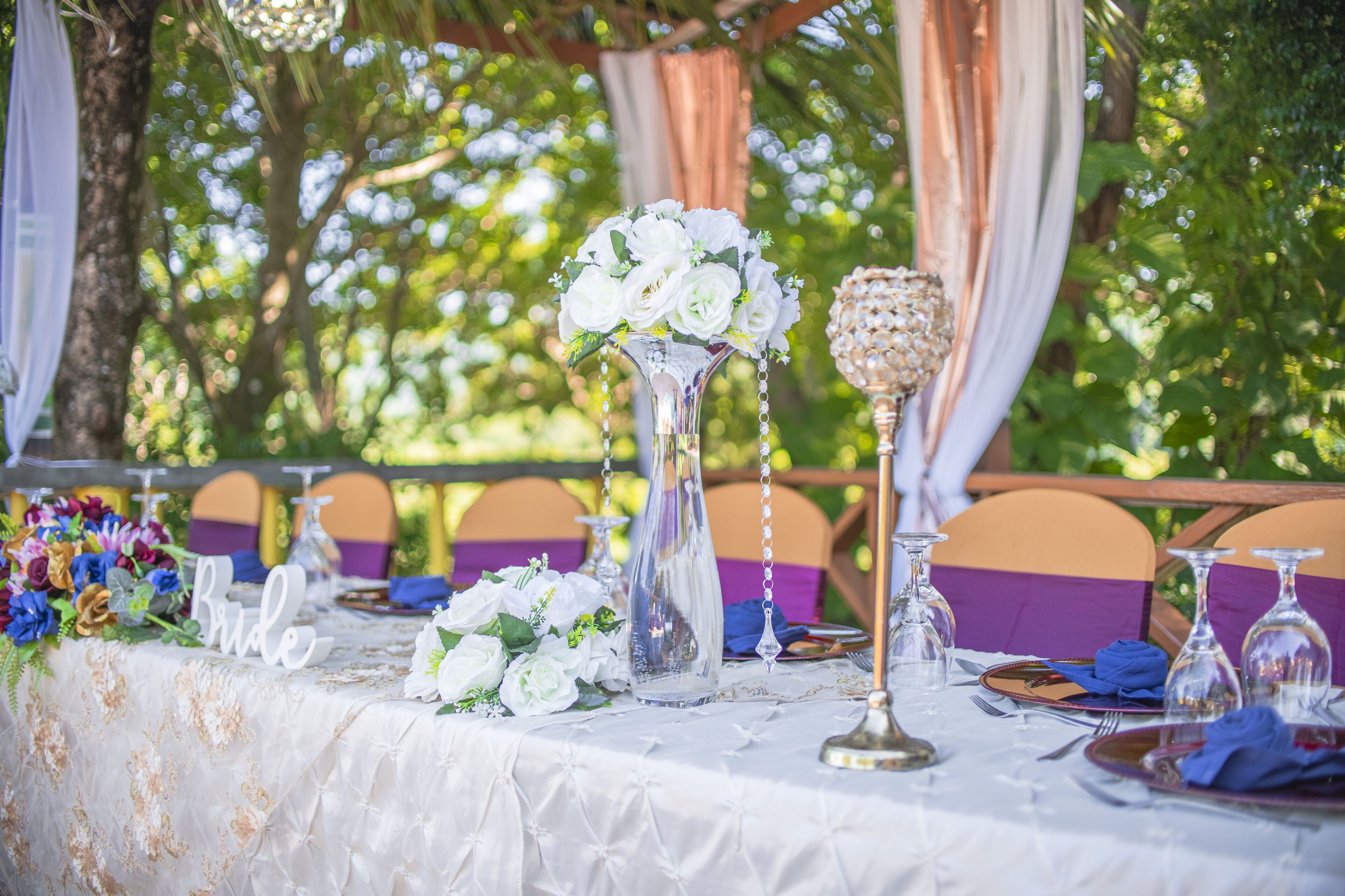 A table set for a wedding reception with a white tablecloth, floral arrangements, and glassware.