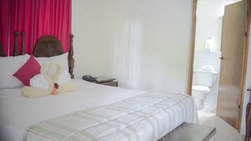 Cama bem arrumada com colcha listrada, cabeceira de madeira e travesseiro rosa.