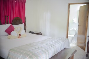 Cama bem arrumada com colcha listrada, cabeceira de madeira e travesseiro rosa.