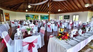 Un salón de banquetes con mesas redondas, manteles blancos y lazos rojos.