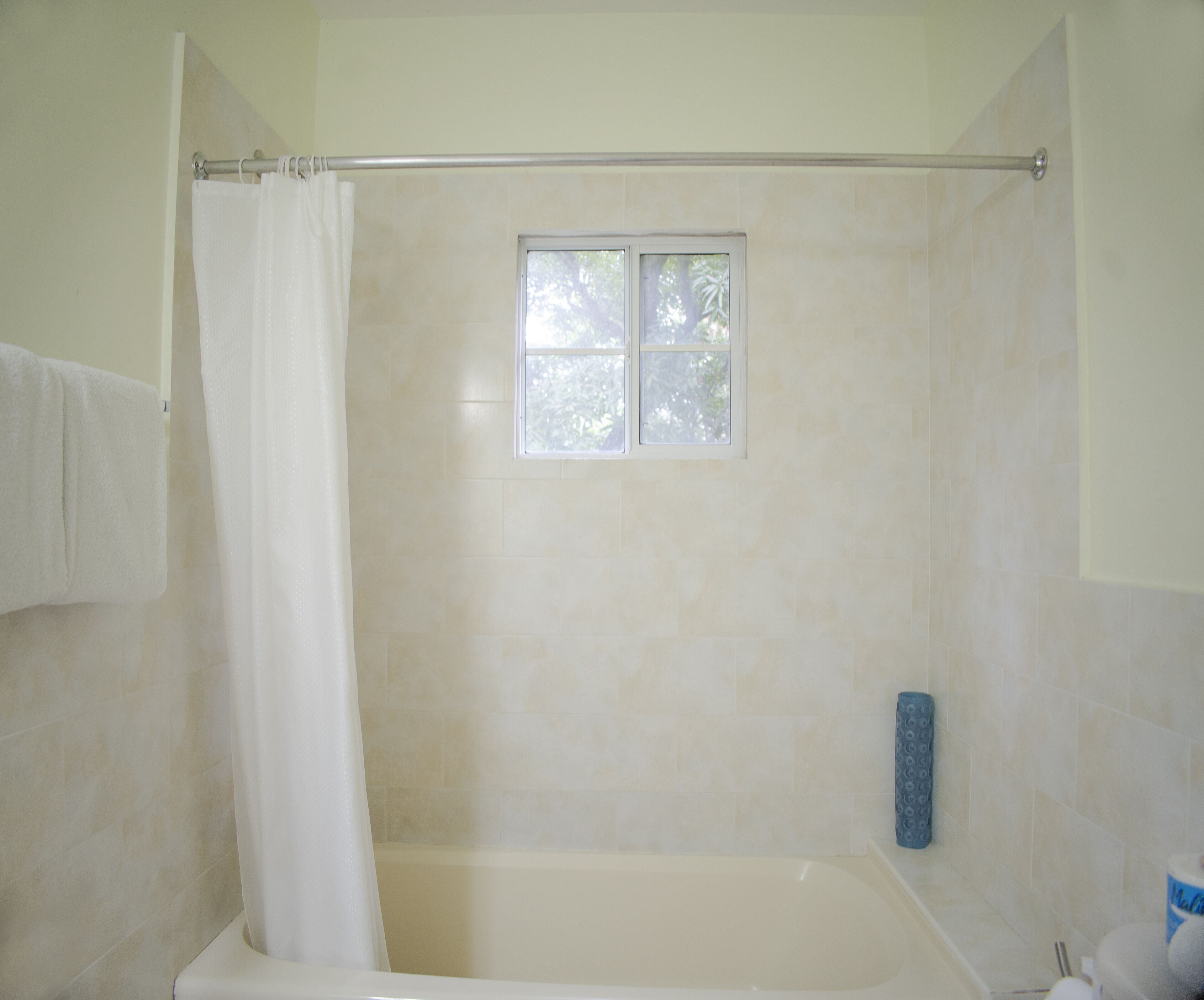 Een badkamer met een bad, douchegordijn, raam en toilet.