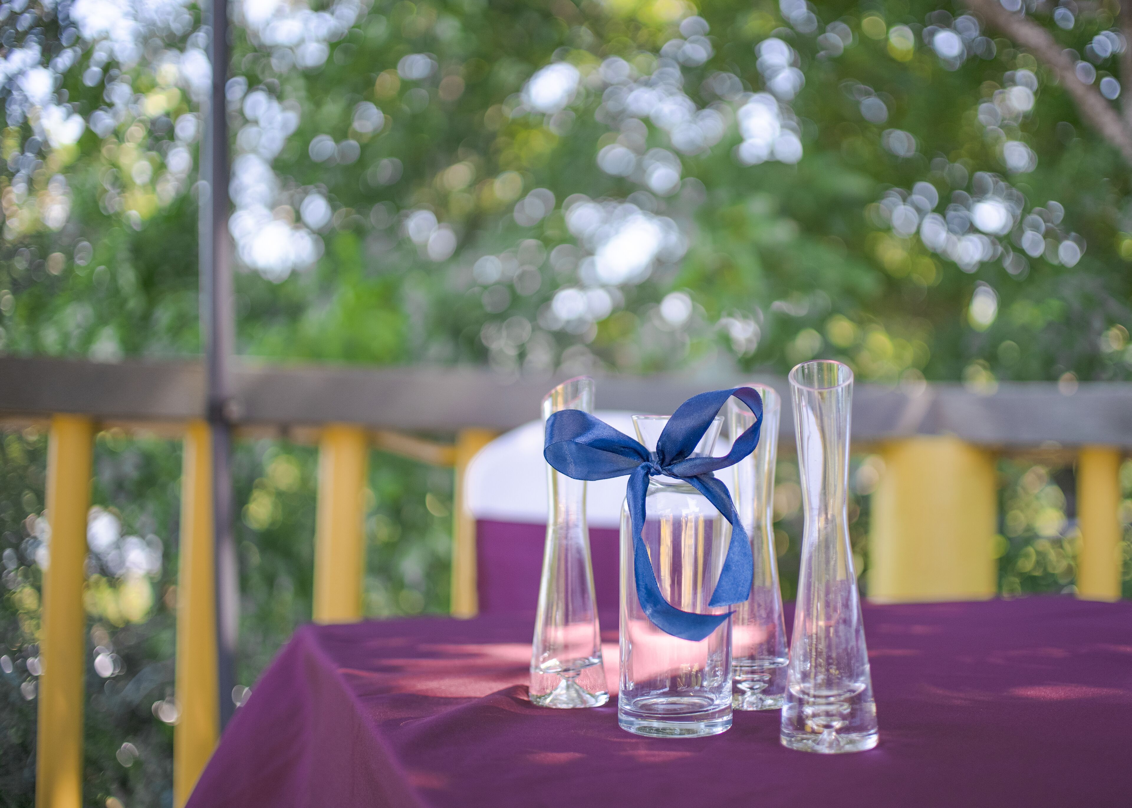 Three clear glass vases with a blue ribbon tied around one, placed on a table with a purple tablecloth.