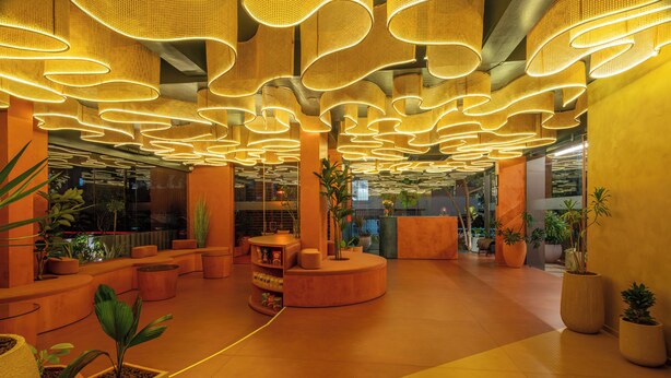 Eine moderne Lobby mit einer gebogenen Rezeption, mehreren Sitzbereichen und einer Decke mit einzigartigen Leuchten.