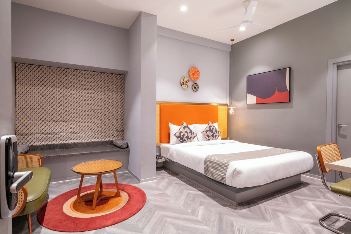 Una habitación de hotel moderna con una cama grande, una zona de estar con una mesita y sillas, un muro decorativo y un ventilador de techo.