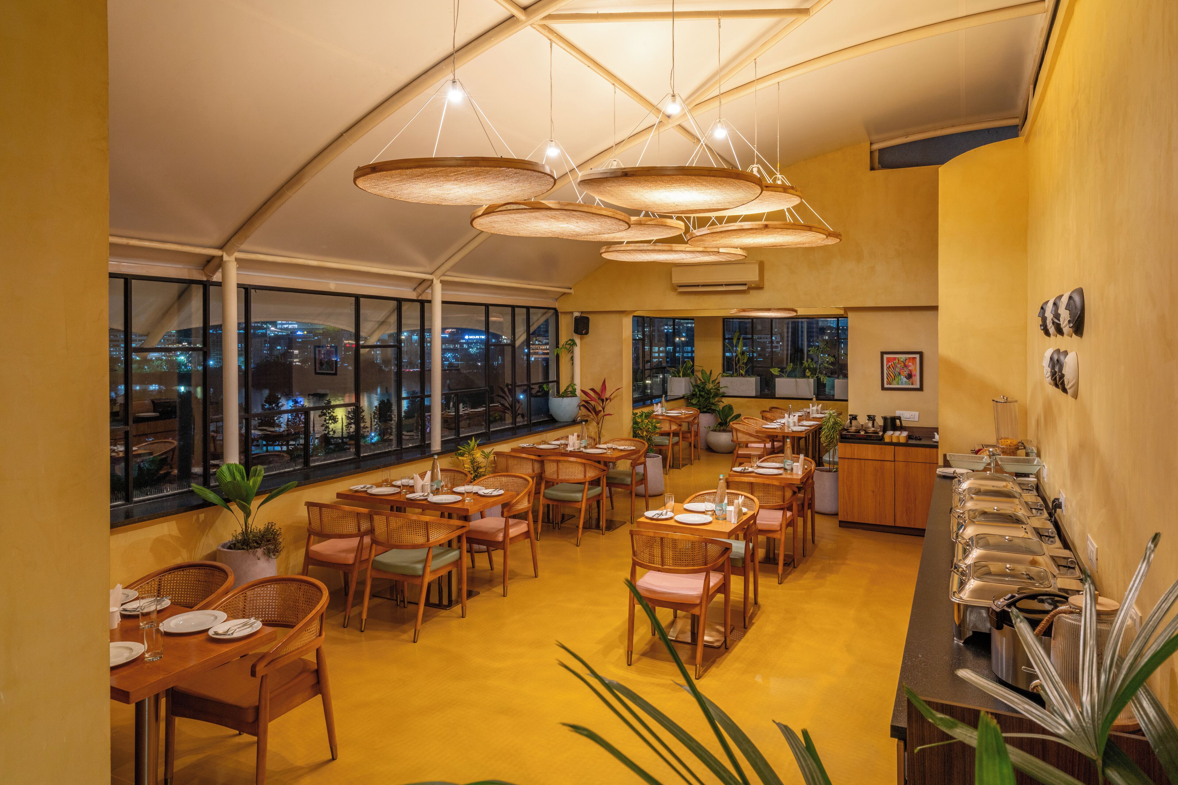 A restaurant with a high ceiling, multiple hanging light fixtures, and a buffet line with various food stations.