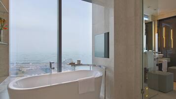 A modern bathroom with a freestanding bathtub, a glass shower enclosure, and a view of the cityscape and water body.