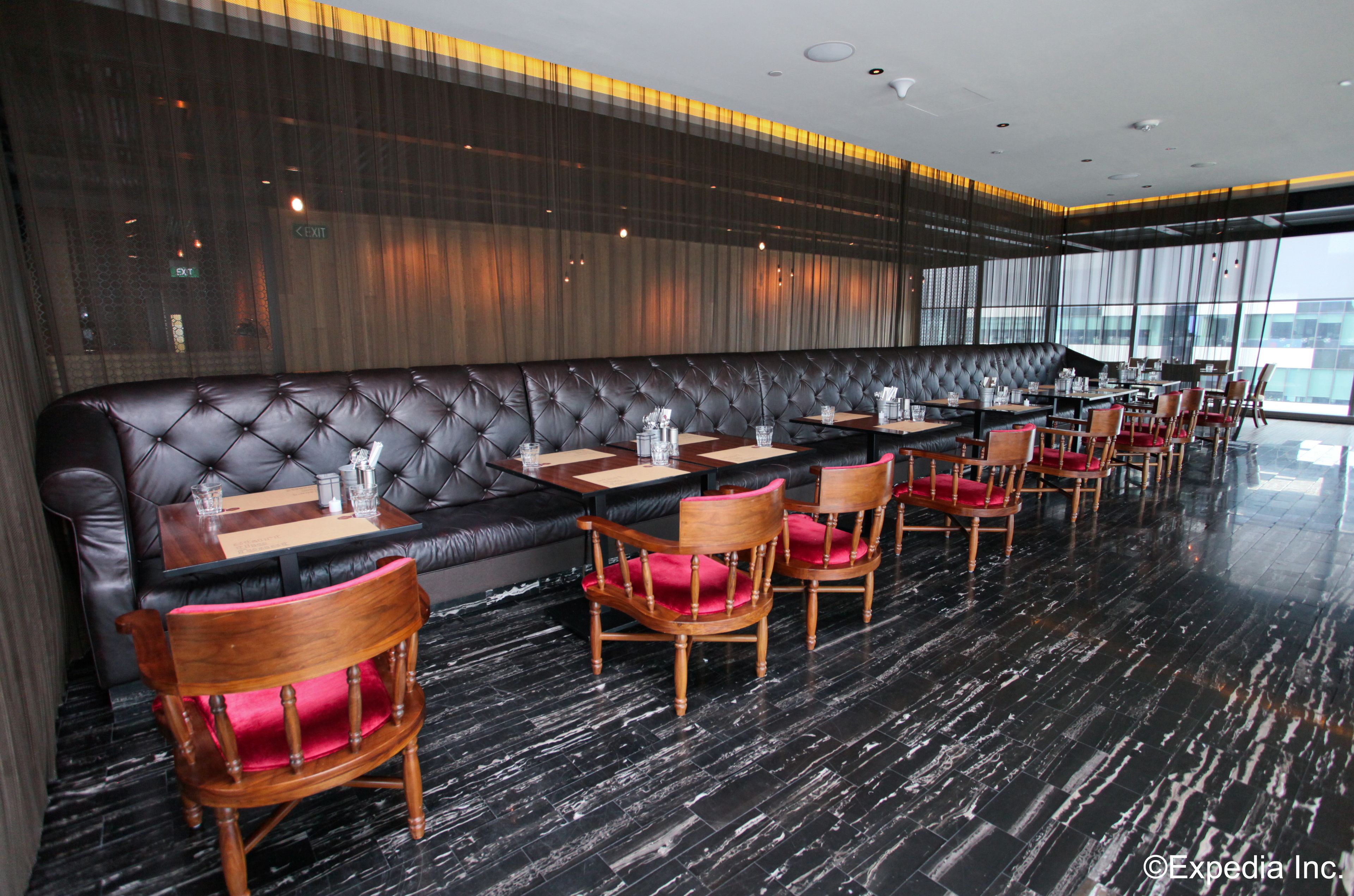Un restaurante moderno con una zona de asientos en una banqueta de cuero negro, mesas de madera y sillas con cojines rojos.