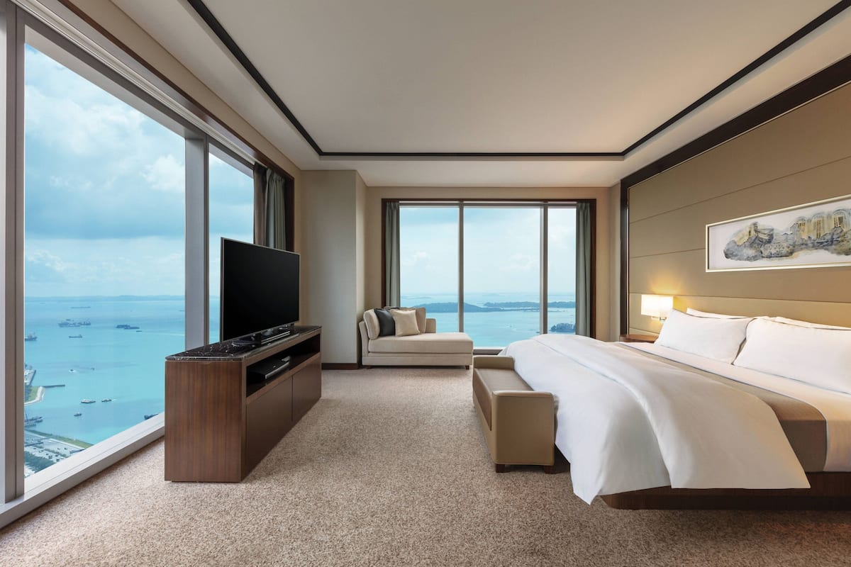 Une chambre d’hôtel avec une grande fenêtre, un lit, un canapé, une télévision et un tableau au mur.