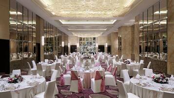 A banquet hall with round tables, white chairs, and floral centerpieces.