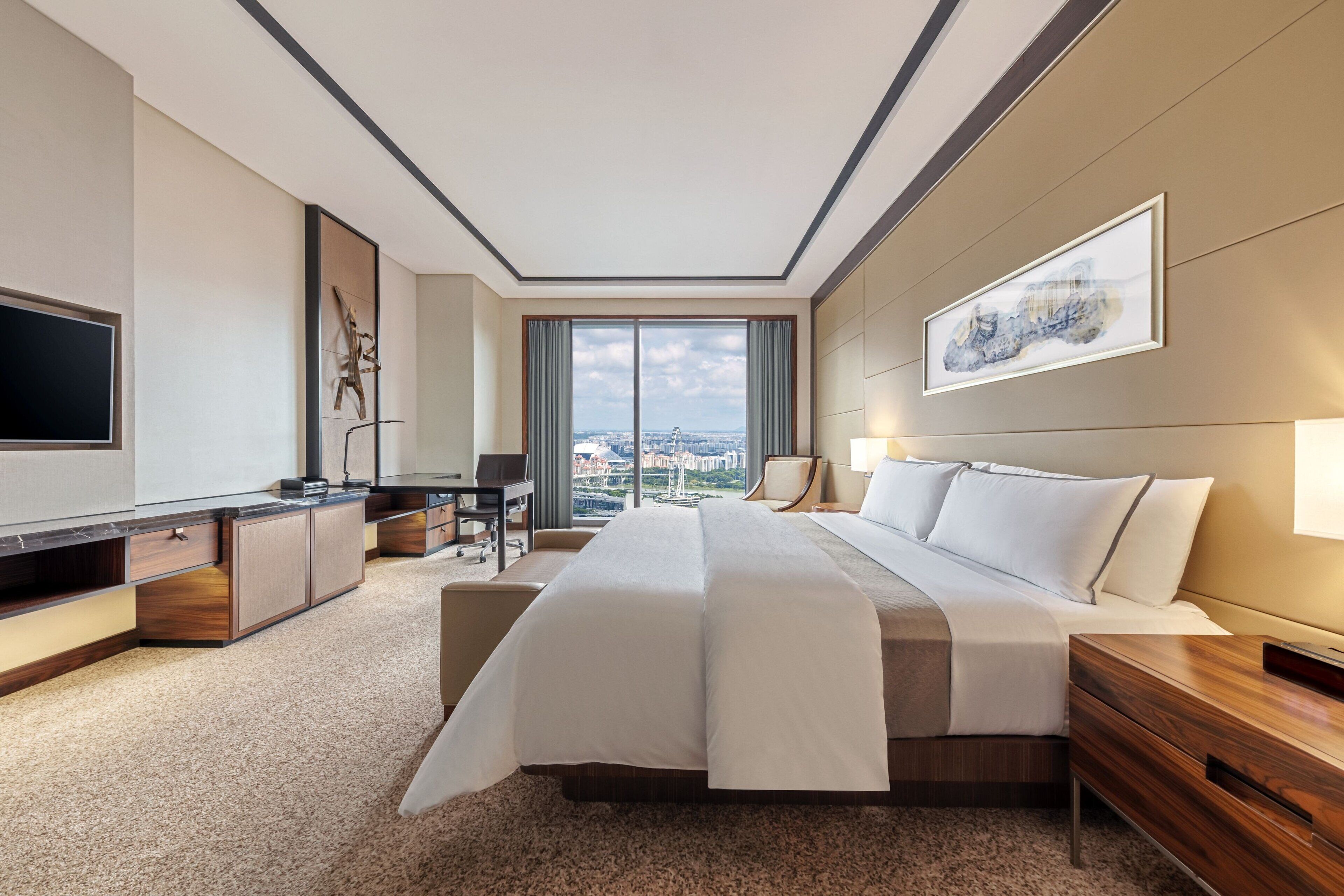 A modern hotel room with a large bed, a desk, a TV, and a view of the city.