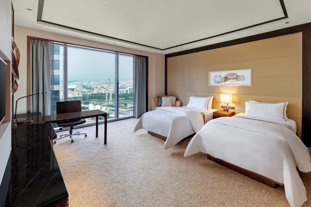 Une chambre d’hôtel dotée d’une grande fenêtre donnant sur la ville, de deux lits, d’un bureau et d’une télévision.