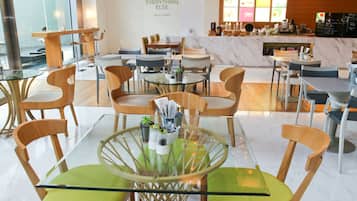 A modern restaurant interior with glass tables, wooden chairs, and a marble counter.