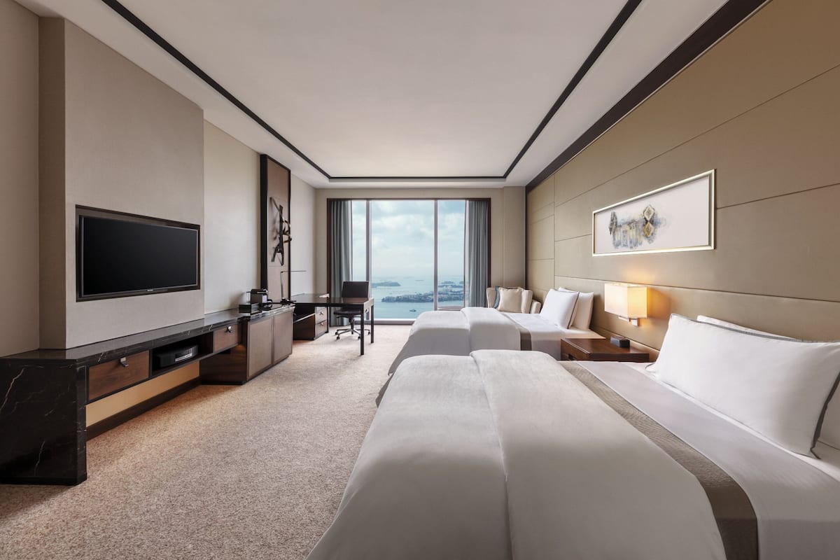 Une chambre d’hôtel moderne dotée d’une grande télévision, d’un bureau, de deux lits et offrant une vue sur la mer.