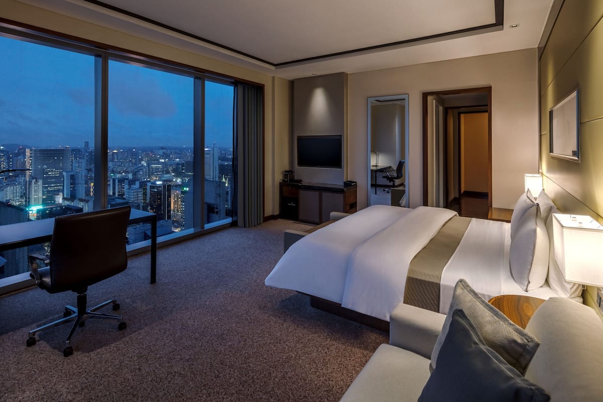 Une chambre d’hôtel avec un grand lit, un bureau, une chaise, une télévision et une vue sur le paysage urbain.