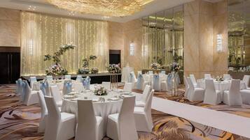 Un salón de banquetes con mesas redondas, sillas blancas y centros de mesa florales.