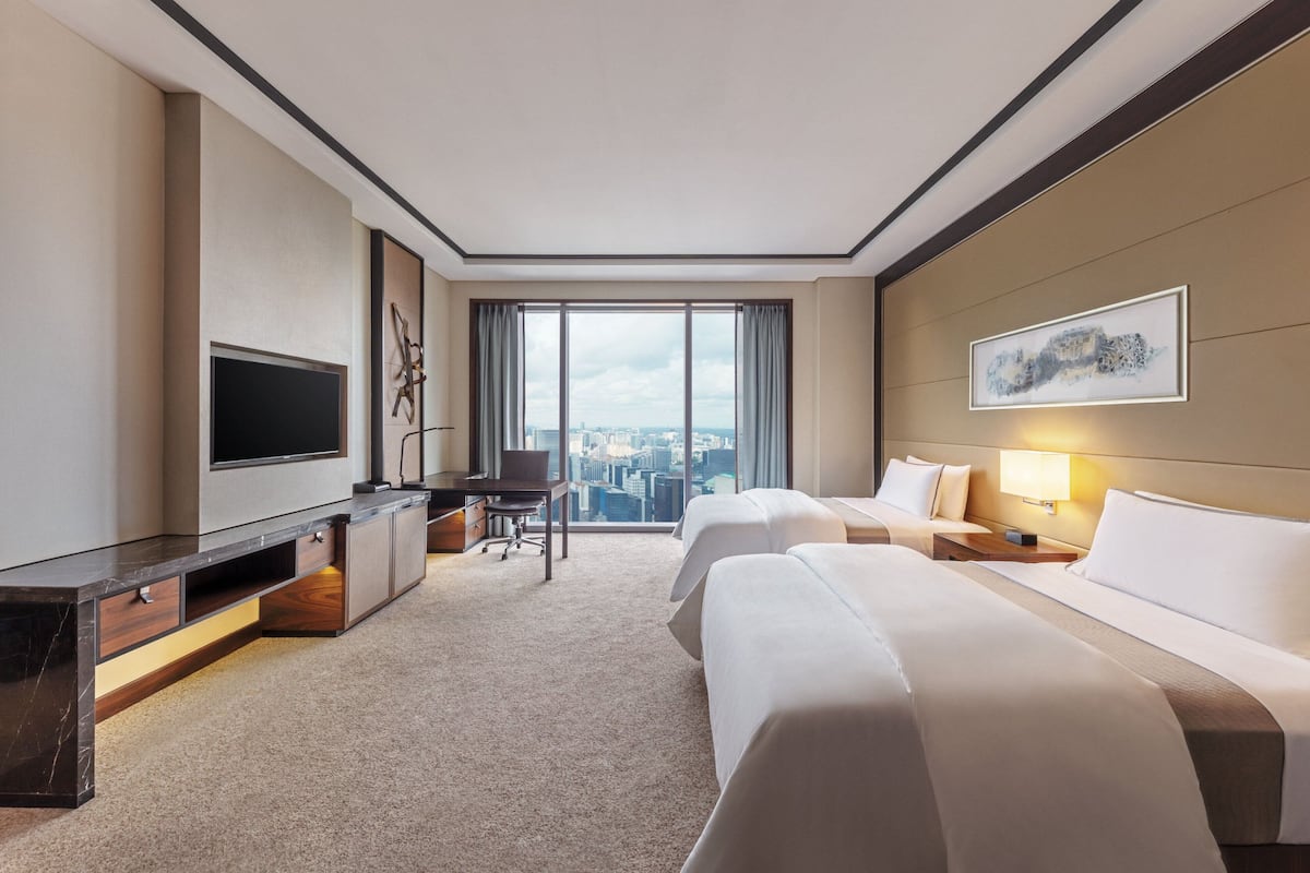 Une chambre d’hôtel dotée d’une grande fenêtre, d’un téléviseur à écran plat, d’un bureau, de deux lits et offrant une vue sur la ville.