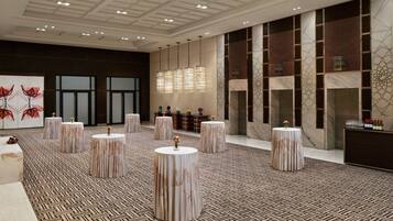 A spacious lobby with a patterned floor, multiple round tables, and a modern reception area with a marble wall and decorative lighting.