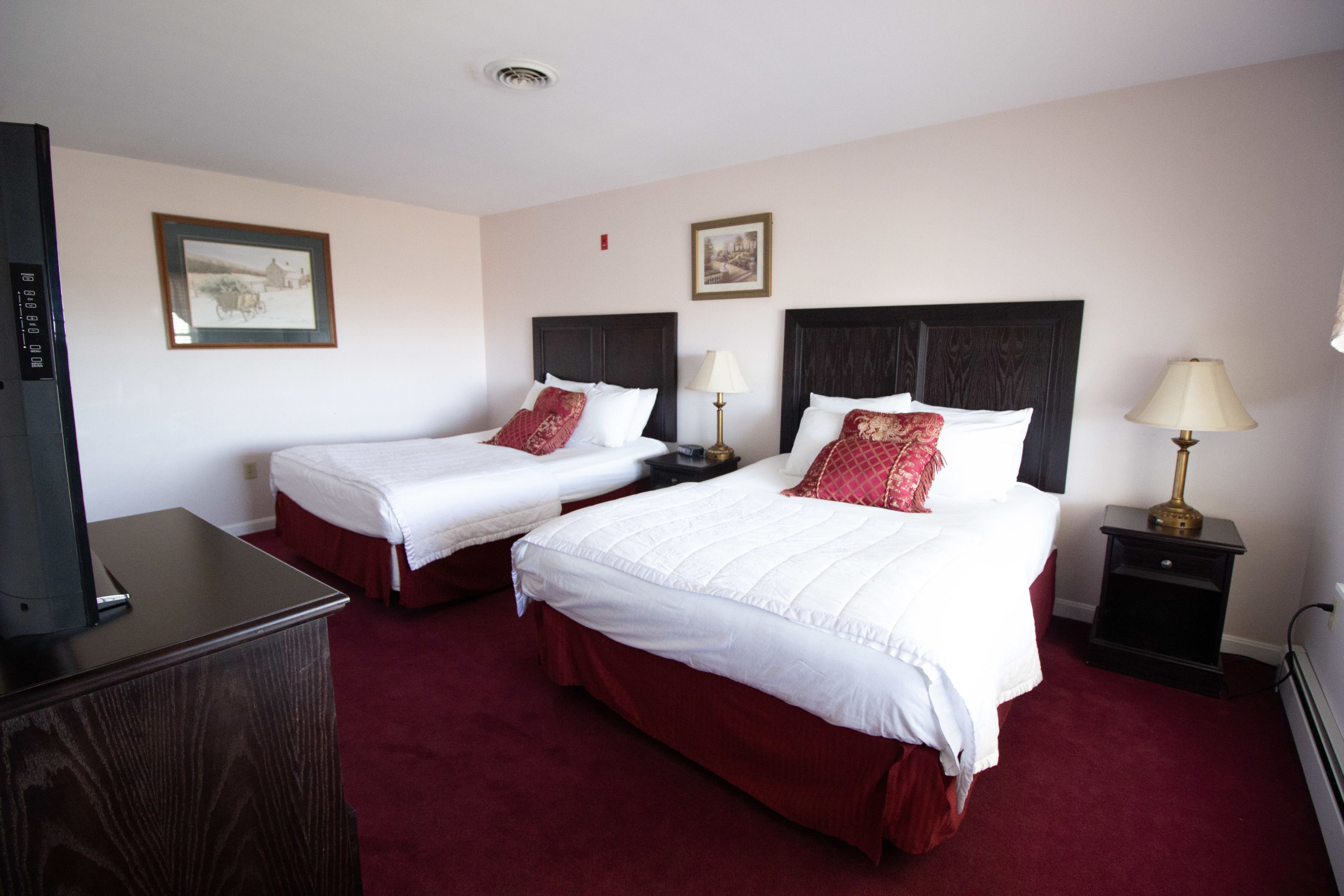 Quarto de hotel com duas camas, televisão e escrivaninha.