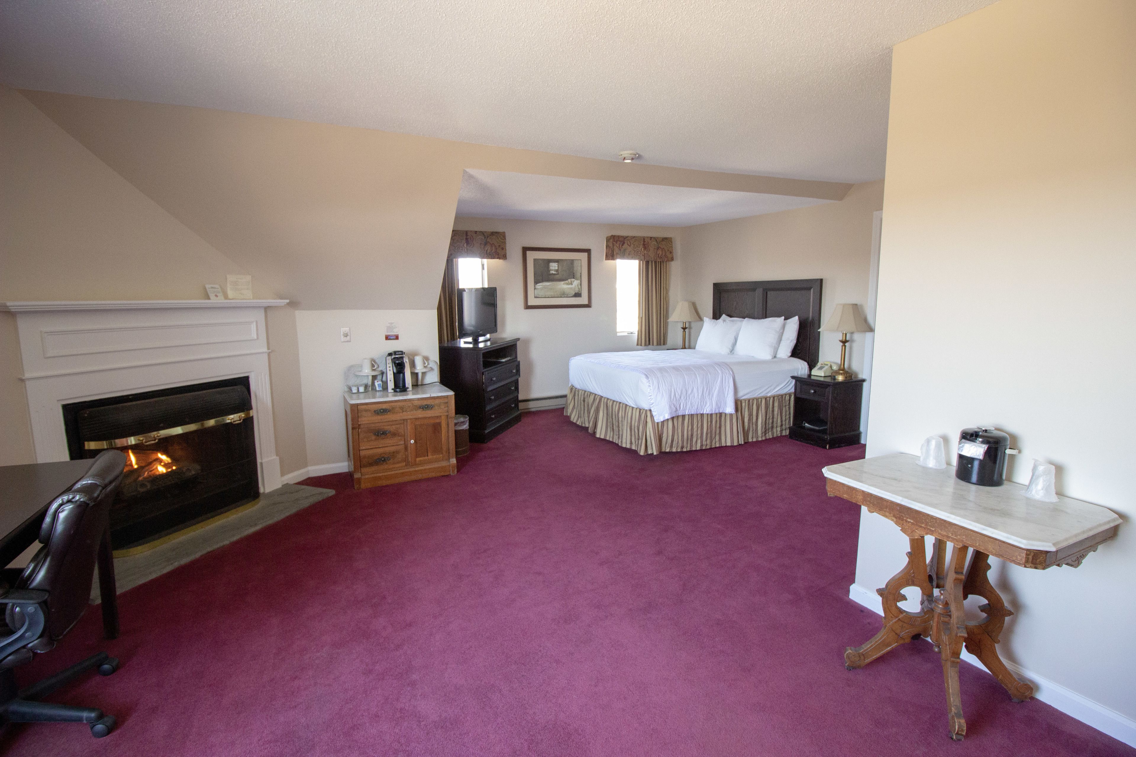 A hotel room with a fireplace, a bed, a desk, and a small table.