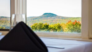 A room with a view of a hill and autumn foliage through a window.