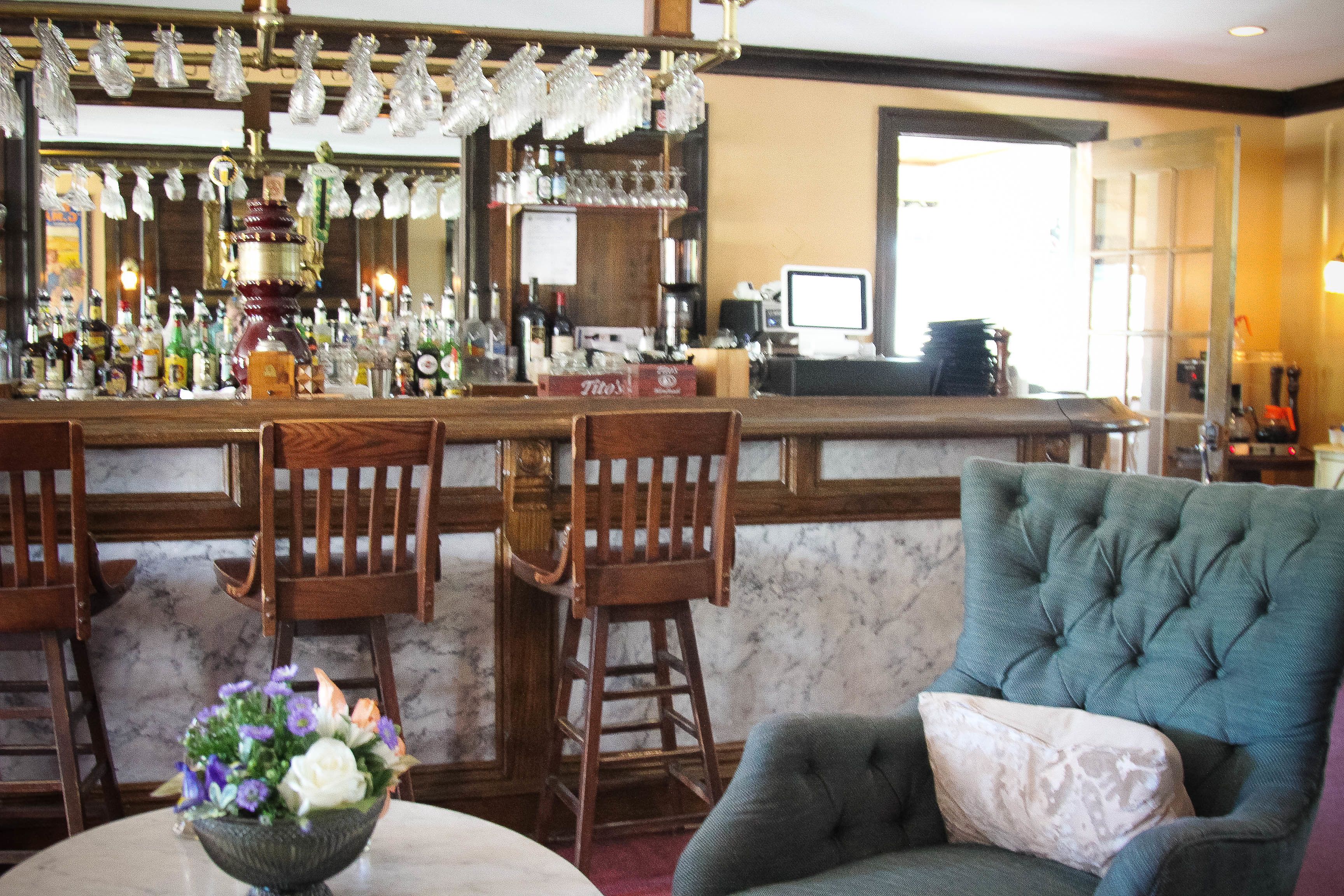 A bar area with wooden chairs, a bar counter, and a large green armchair with a cushion.