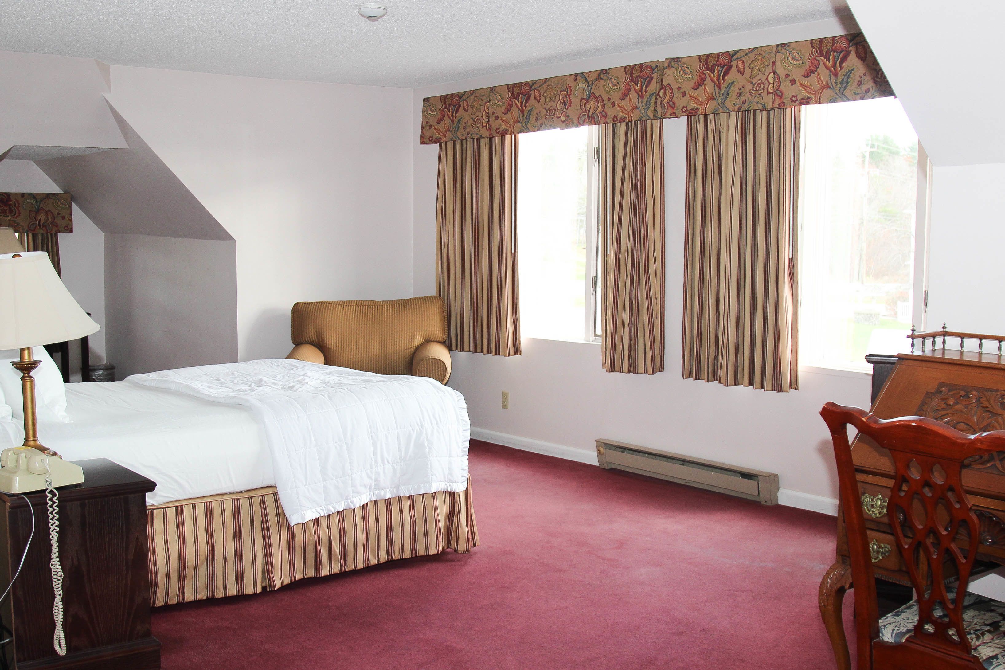 A hotel room with a bed, a chair, a desk, and a telephone.