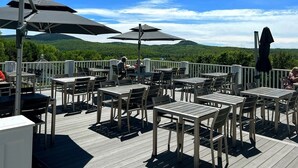 An outdoor deck with tables and chairs, umbrellas, and a view of green hills.