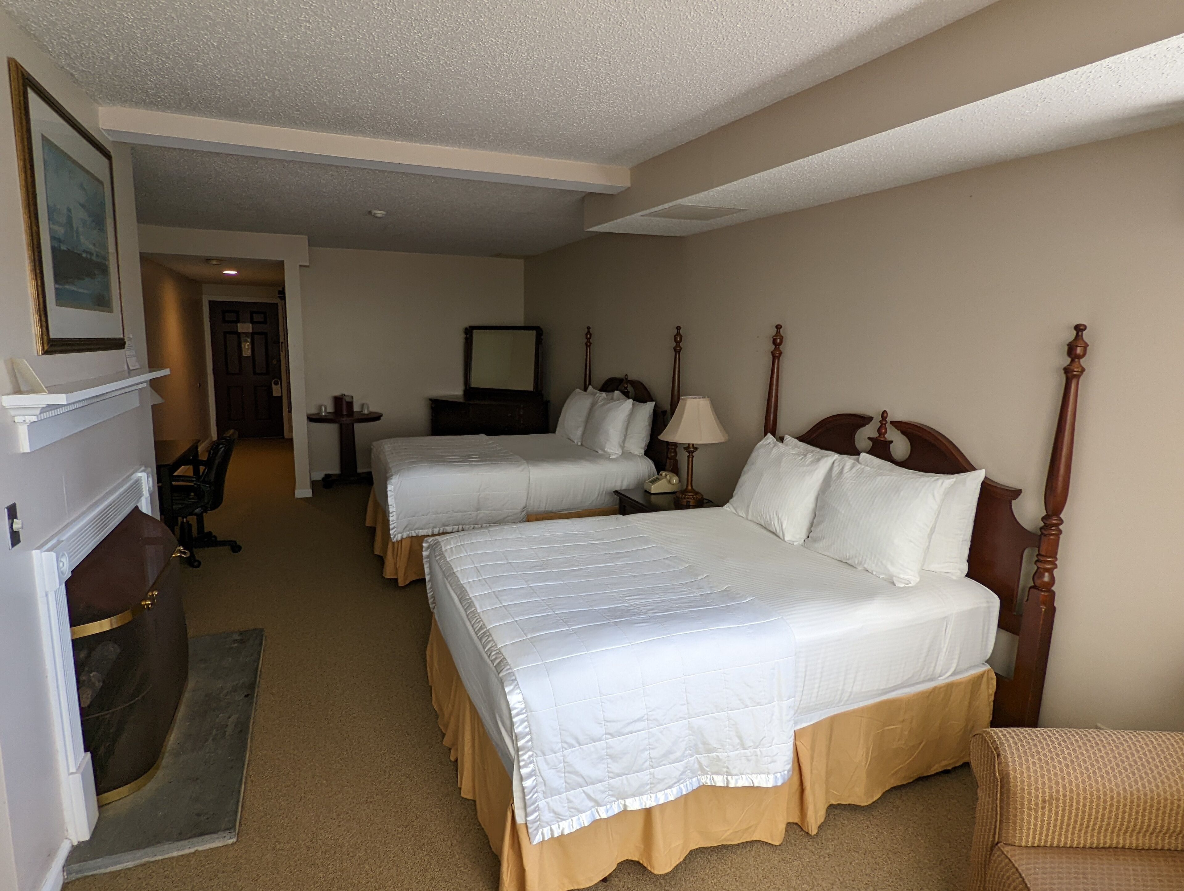 Een hotelkamer met twee bedden, een bureau, een stoel, een spiegel en een open haard.