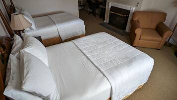 A hotel room with two single beds, a wooden headboard, a chair, a fireplace, and a small table with a lamp.