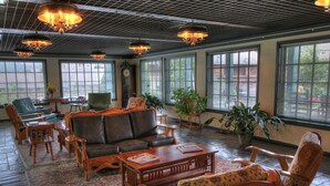 A spacious lobby with a large leather sofa, wooden chairs, a coffee table, and large windows with blinds.