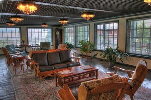 A spacious lobby with a large leather sofa, wooden chairs, a coffee table, and large windows with blinds.