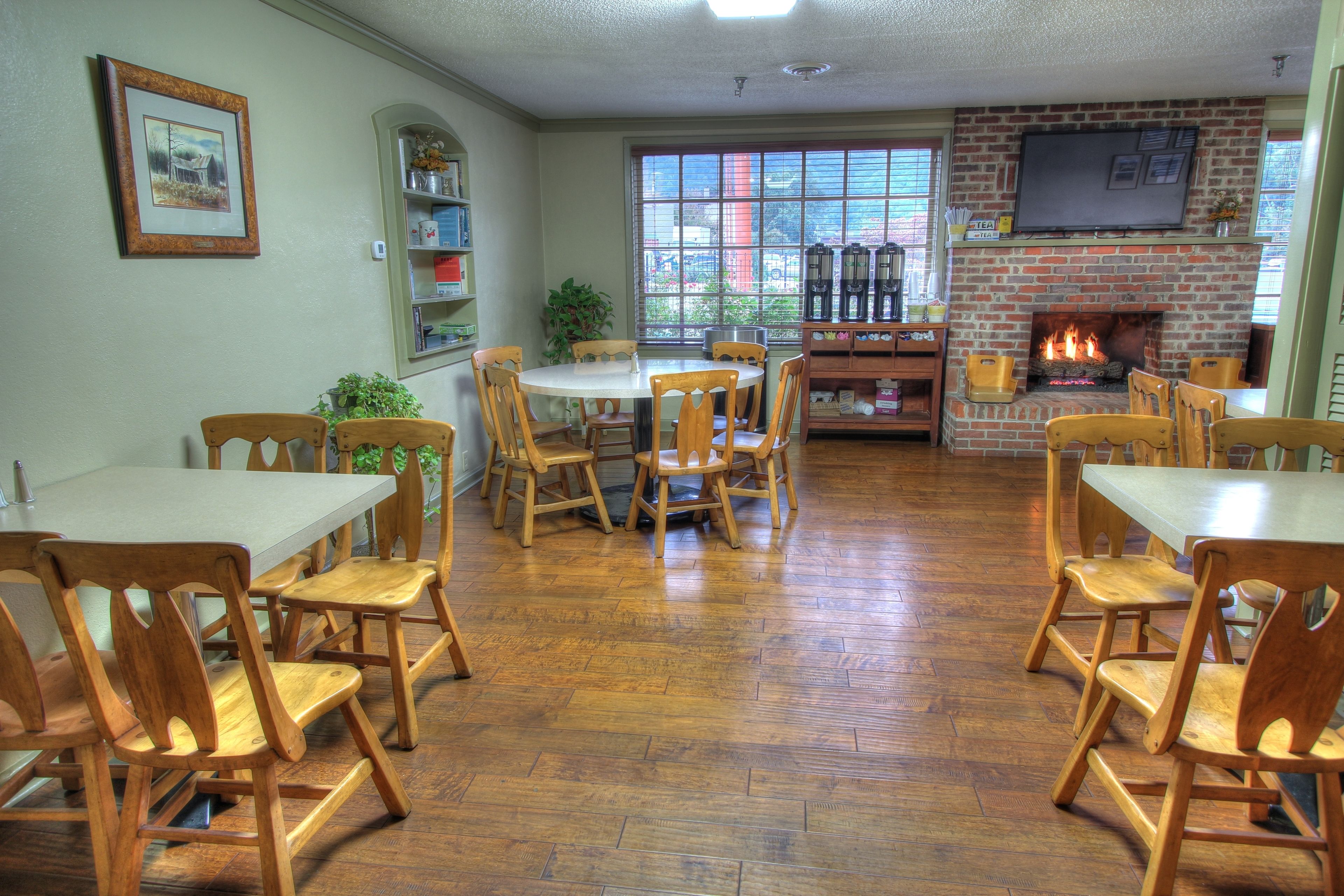 A dining area with wooden tables and chairs, a brick fireplace, and a large window with a view of the outside.