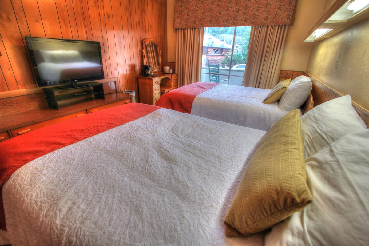 A hotel room with two beds, a television, and a window with curtains.