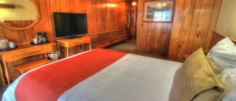 Habitación de hotel con decoración de madera, una cama grande con cubrecama rojo y blanco, televisión, escritorio con cafetera y un cuadro en la pared.